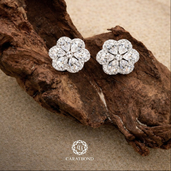 Flower-shaped diamond earrings on a wooden surface with CARATBOND logo.